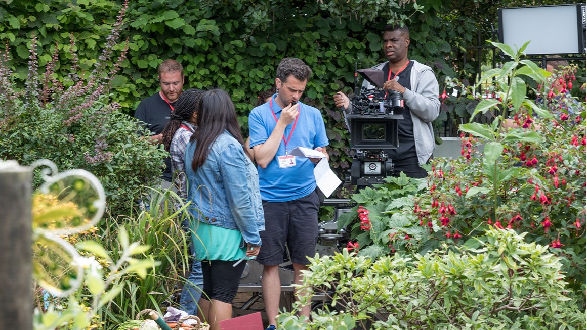 Still of crew working on set in between bushes