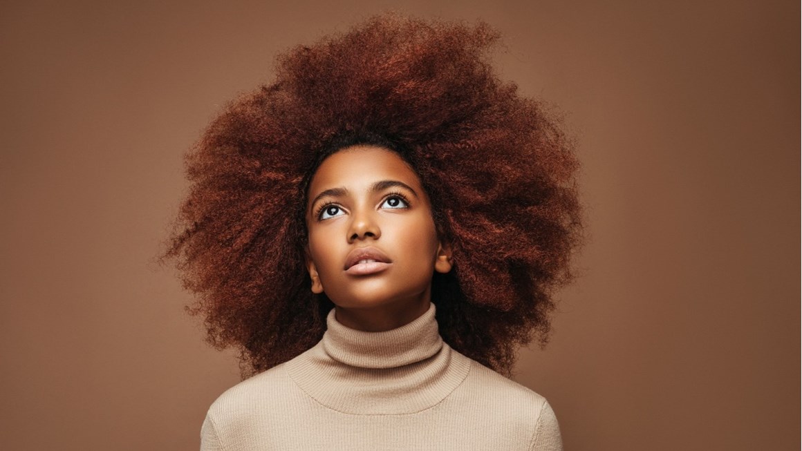 Striking head shot of a Black female model shot against a brown/bronze background. She wears her hair in a natural, textured style.
